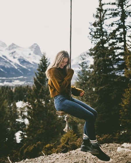 A picture of Jordan Claire Robbins swinging near the beautiful scenery of mountain.